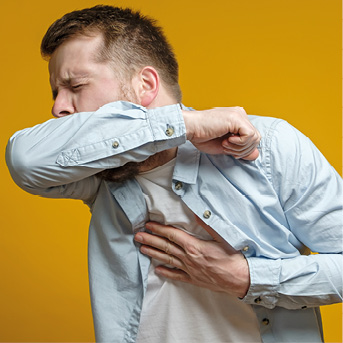 Man coughs in his elbow and holds hand on chest, experiencing pain. Correct sneezing. Concept of spread of the virus.